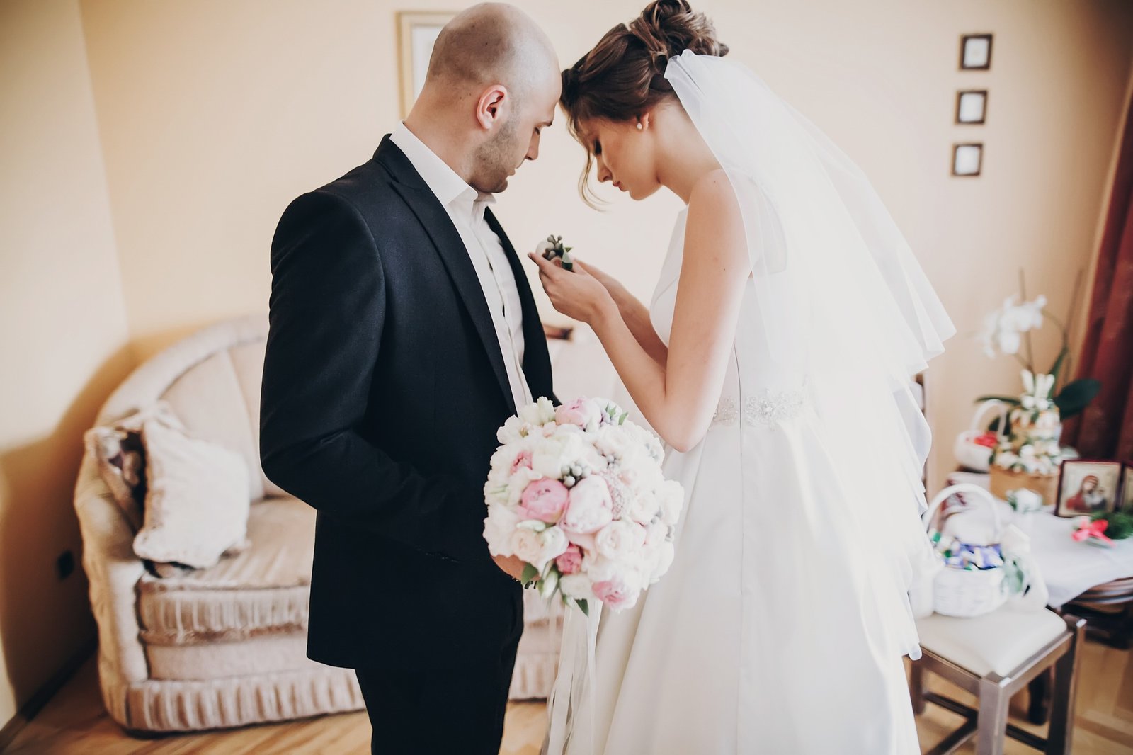 Beautiful bride putting stylish boutonniere on groom suit