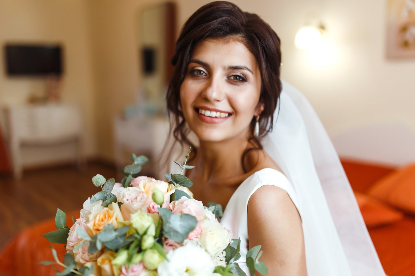 Morning of bride. Beautiful smiling brunette bride in white dress with wedding bouquet in her hands.